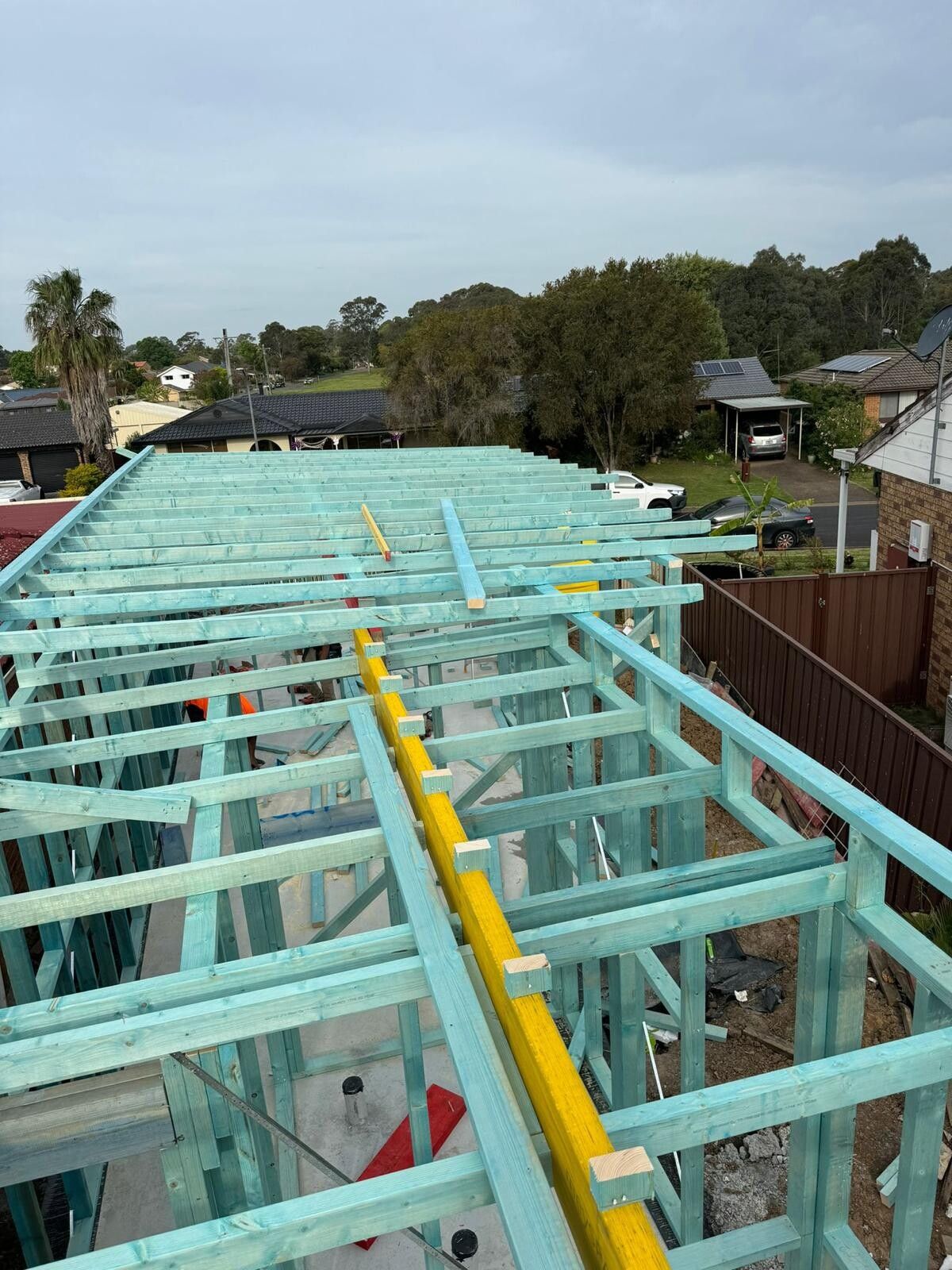 View along floor joists and wall frames with a yellow LVL beam, looking over a suburban street